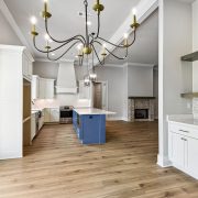 The adjacent kitchen boasts a blue island with marble countertops, white cabinetry, and open shelving, blending functionality with modern elegance.