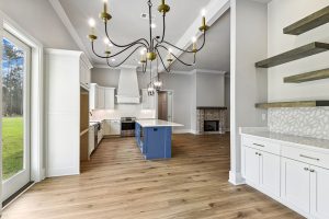 The adjacent kitchen boasts a blue island with marble countertops, white cabinetry, and open shelving, blending functionality with modern elegance.