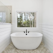 The room is bathed in natural light from the large window near the freestanding tub, which offers a serene view of the surrounding nature.