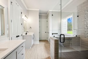 The room includes dual vanities with ample storage and sleek fixtures, complemented by a soothing neutral color palette and natural light from the window.