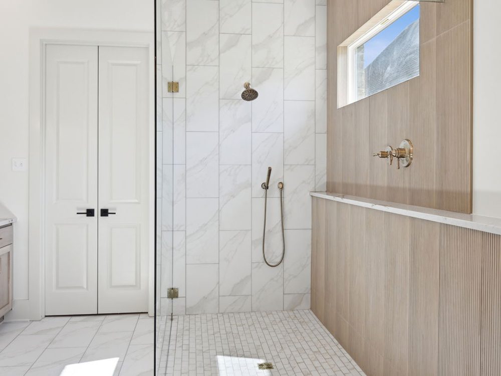 This spa-inspired walk-in shower exudes modern elegance and thoughtful design. The walls feature a striking combination of large-format porcelain tiles with subtle marble veining and warm, vertical wood-look panels, creating a clean, organic contrast.