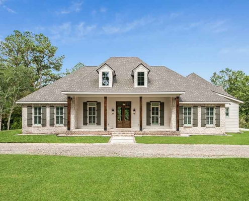 From the street, the home reads as a true Southern classic, with a wide front porch, stained wood columns, twin dormers, and a balanced mix of brick and siding anchored by dark shutters.