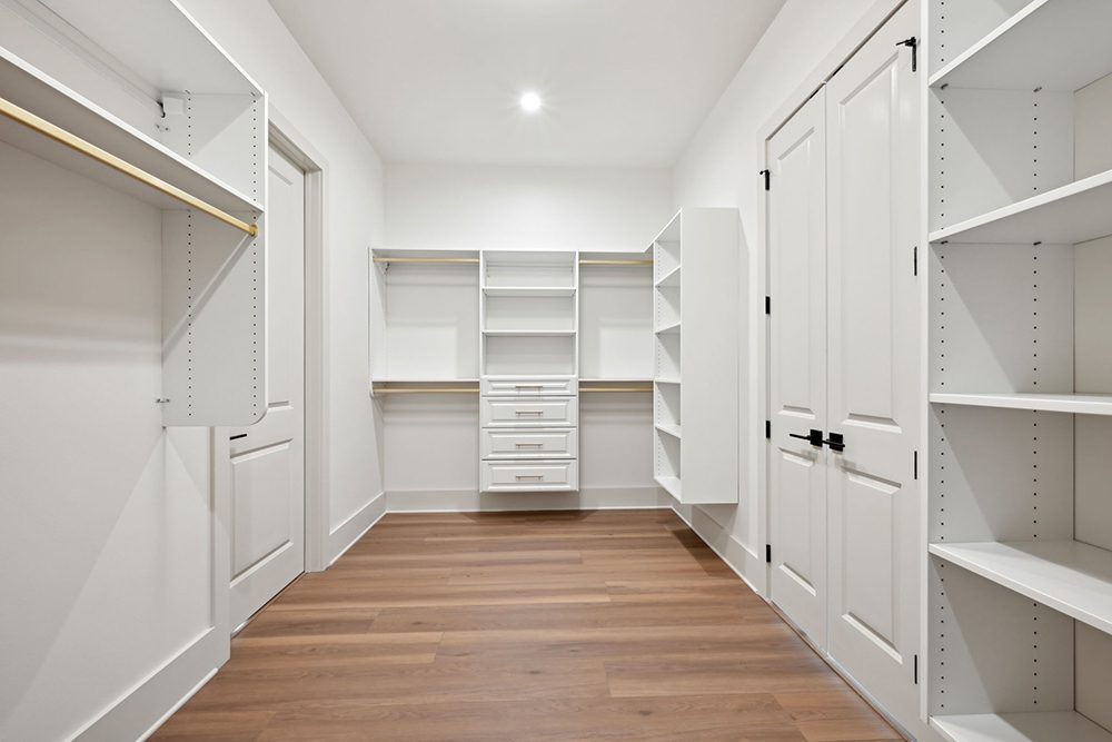 This spacious, custom-designed walk-in closet is the perfect blend of luxury and functionality. Crisp white shelving and built-in cabinetry provide ample storage options for clothing, shoes, and accessories, while sleek gold hanging rods add a touch of sophistication.