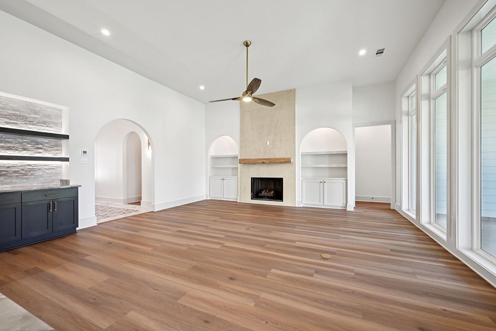 Floor-to-ceiling windows flood the space with natural light, while arched doorways and soft white walls contribute to the room’s elegant and airy ambiance.