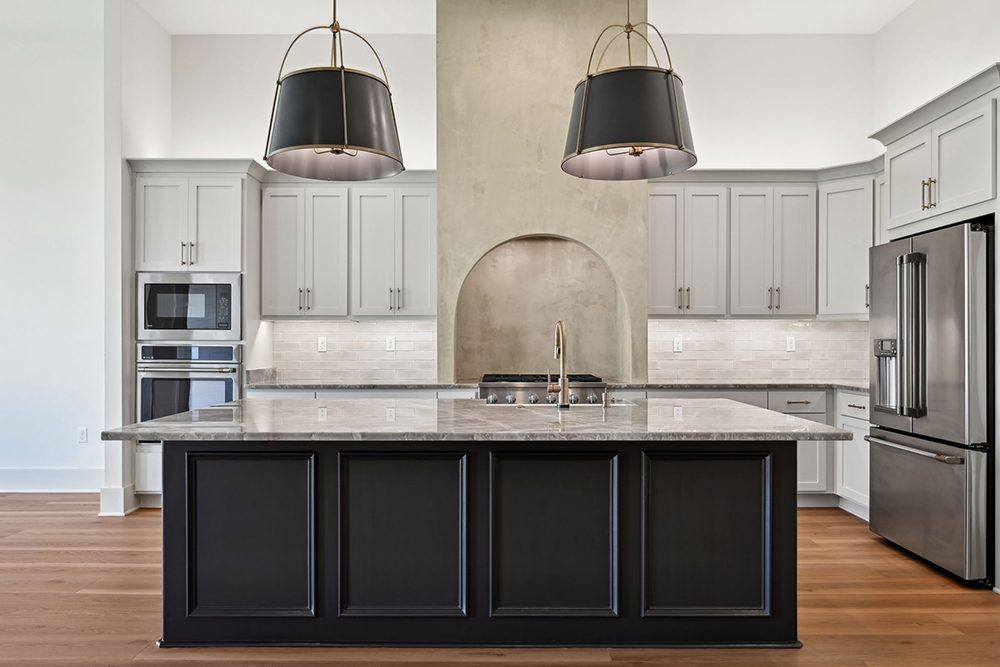 A unique arched niche behind the cooktop draws the eye, flanked by a stylish plaster-style range wall that adds texture and character. The soft taupe subway tile backsplash and under-cabinet lighting create a cohesive and inviting atmosphere, while wide-plank wood flooring grounds the entire space with warmth. This kitchen is not only functional but also a designer showcase—perfect for entertaining or everyday culinary inspiration.