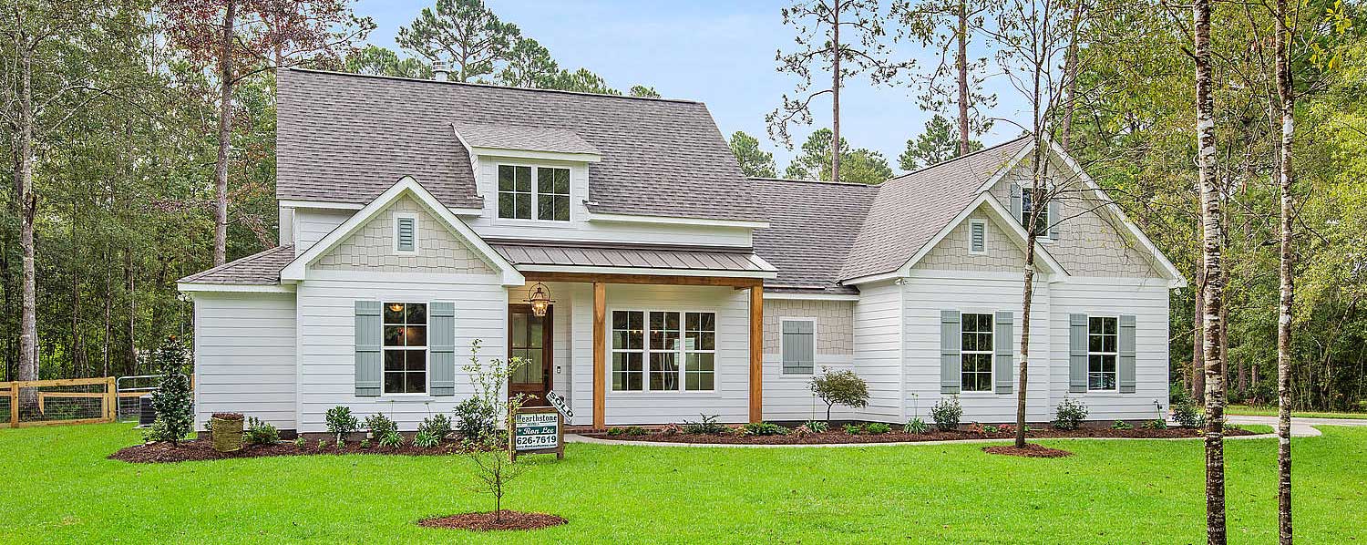 The symmetry of the dormers and gables gives the house a balanced, classic look. The landscaping is clean and natural, blending seamlessly with the wooded backdrop. A “SOLD” sign confirms this serene gem is already claimed.