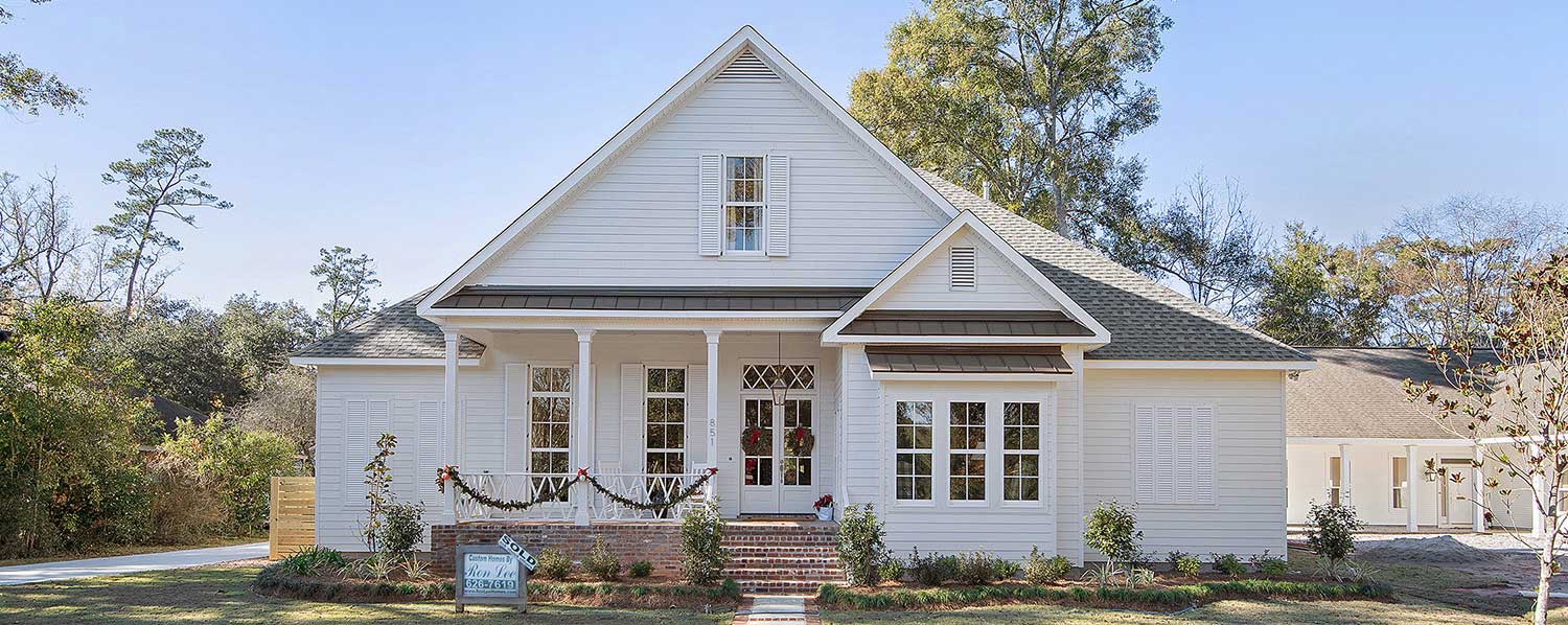 Dormer windows and a metal awning add architectural interest. Lush landscaping surrounds the front path, and a sign confirms this inviting home is already sold.